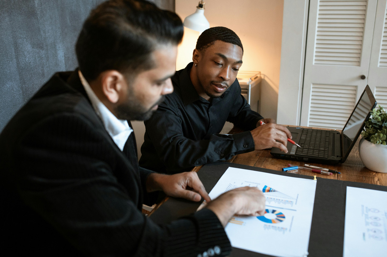 Two men sitting at a desk looking at charts